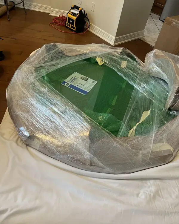 Pool table wrapped in protective plastic and padding on a covered floor, ready to be moved