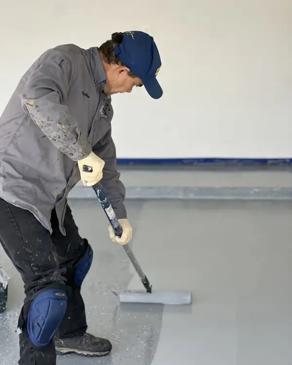 Worker rolling floor coating across a garage slab with a long-handled roller
