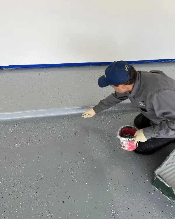 Worker cutting in the edge of a garage floor coating along a taped wall line