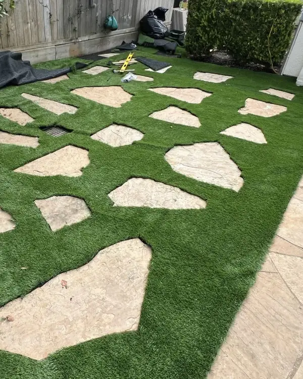 Artificial grass with large flagstone stepping stones set into it, running down the side of a house