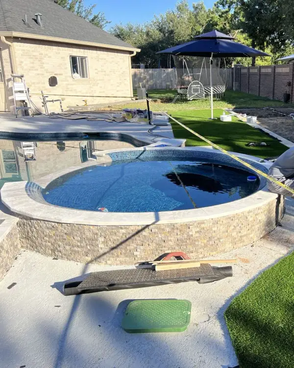 Crew installing artificial grass around a backyard pool with patio umbrellas overhead