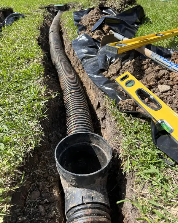 Open trench in a lawn with corrugated French drain pipe and filter fabric ready to be backfilled